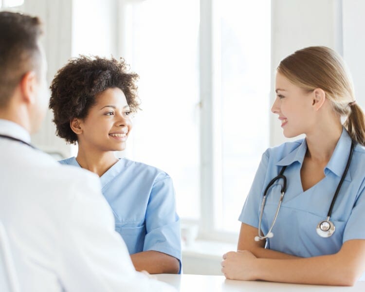 Two Nurses Talking In Front Of Doctor